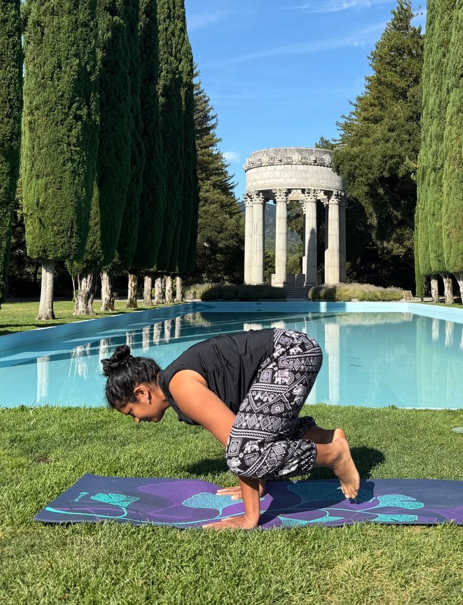 Pushya practicing an arm balance outdoors beside a reflecting pool