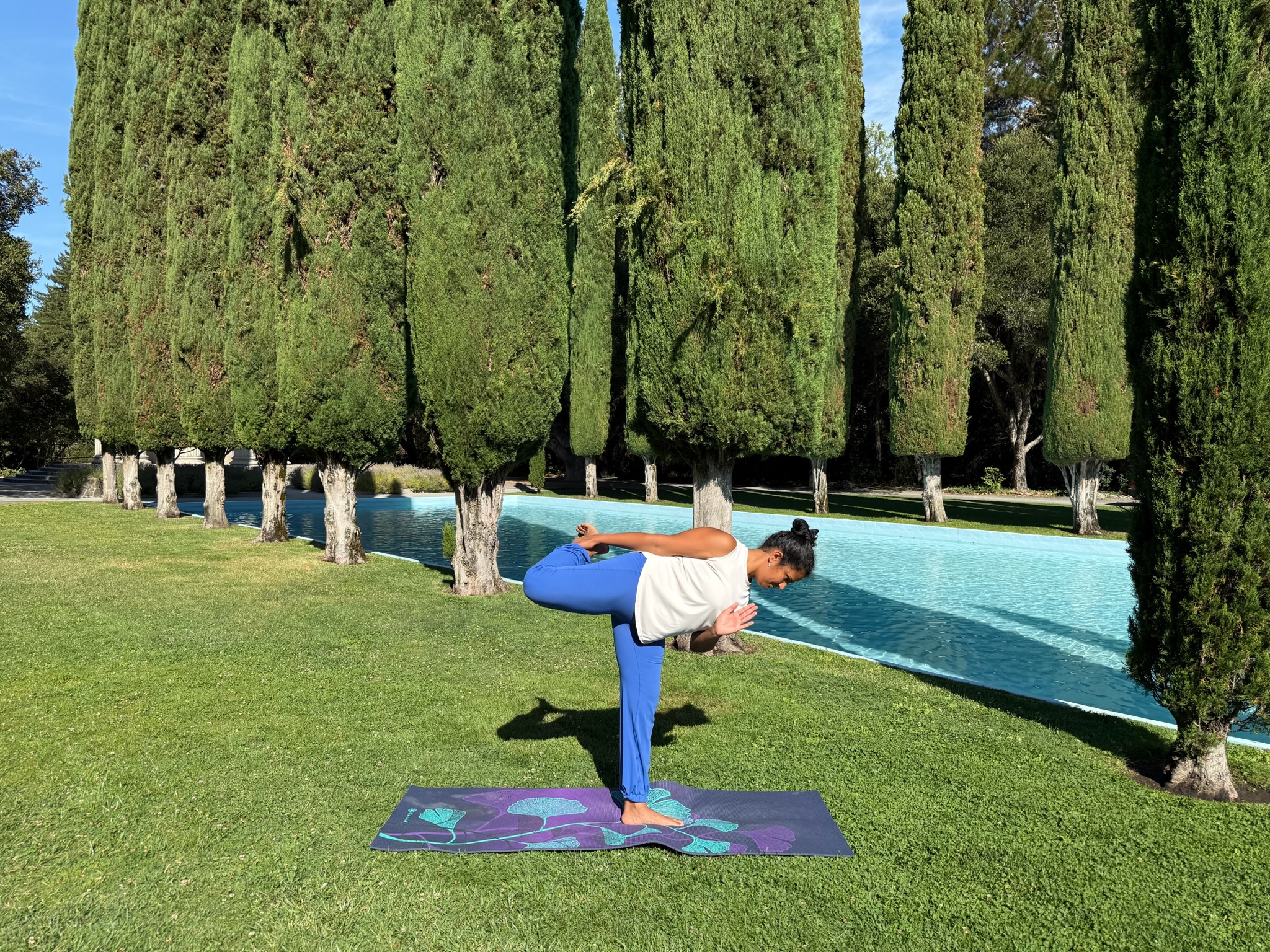 Pushya practicing a standing balance outdoors beside a reflecting pool