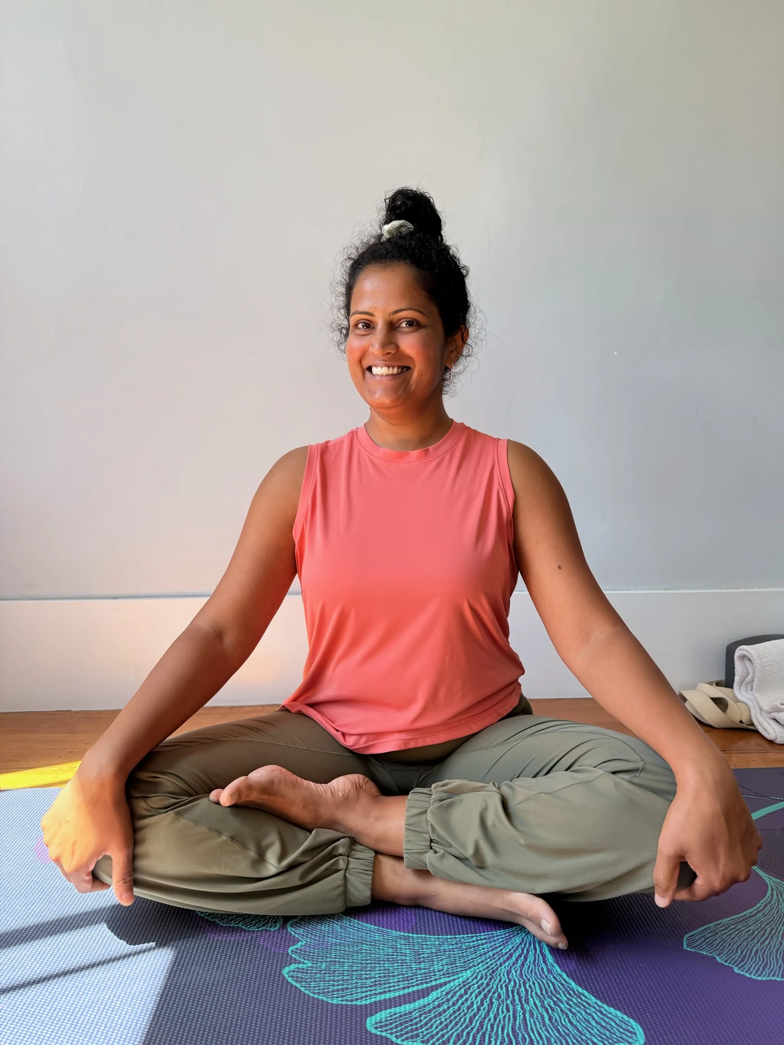 Pushya smiling warmly while seated on a yoga mat